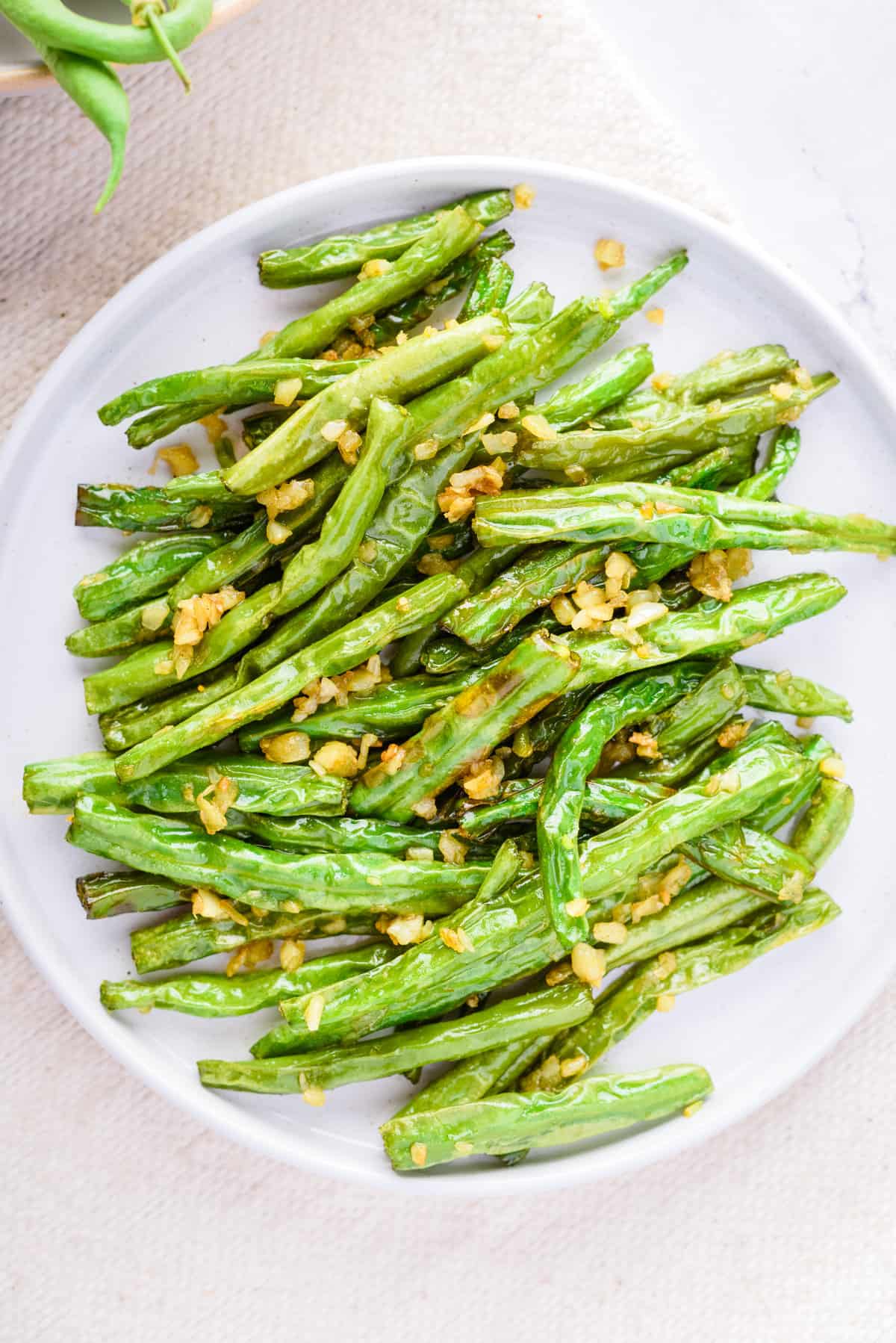 Green beans smothered in garlic, served on a white plate. 