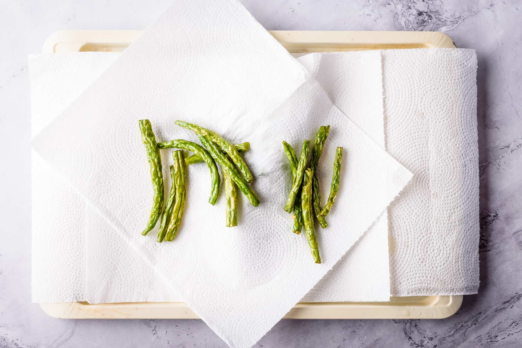 Overhead view of green beans placed on a paper towel on a platter.
