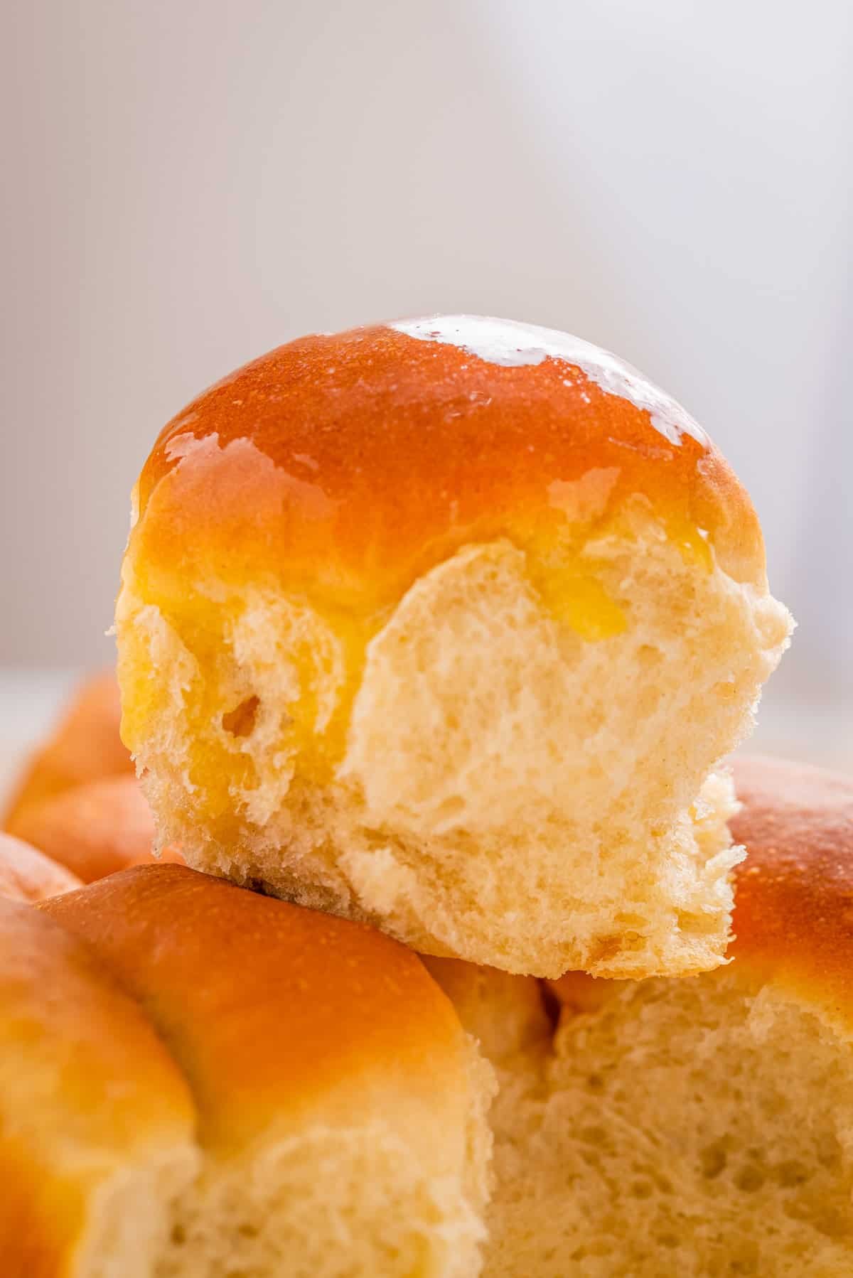 Close up of dinner roll with butter brushed on top, placed on top of other dinner rolls.