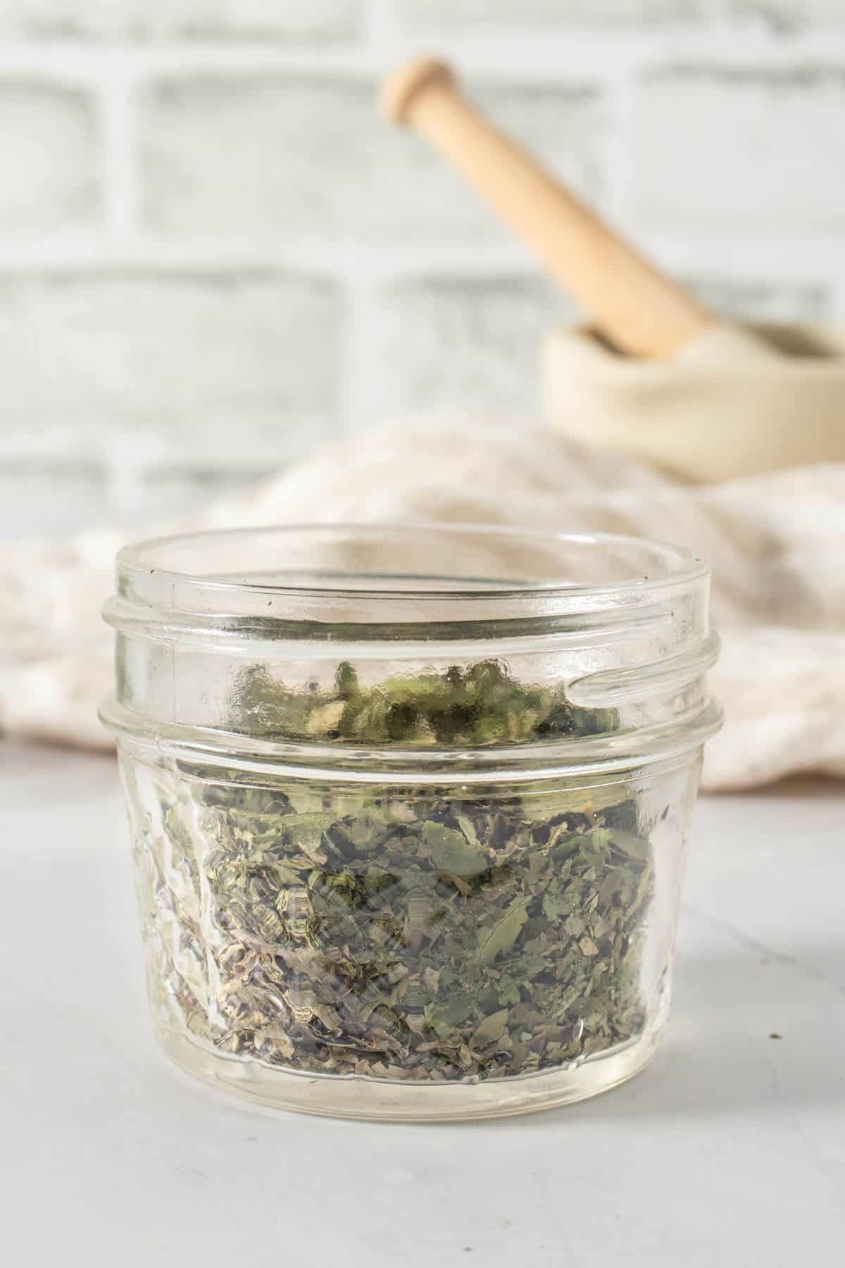 Dried basil in small jar, mortar and pestle in the background
