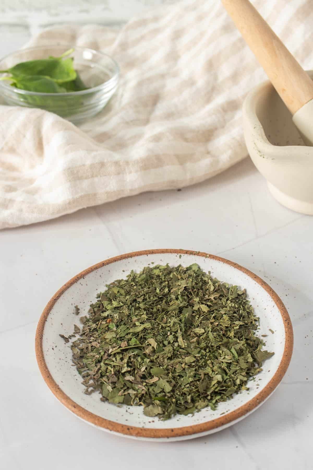 Close up of dried basil on a plate with mortar and pestle in the background 