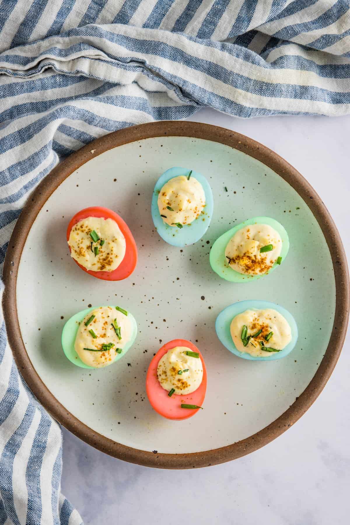 Plate of colored deviled eggs with a blue/white stripe napkin in background.