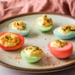 Close up of colored deviled eggs on a plate, with pink napkin in background.