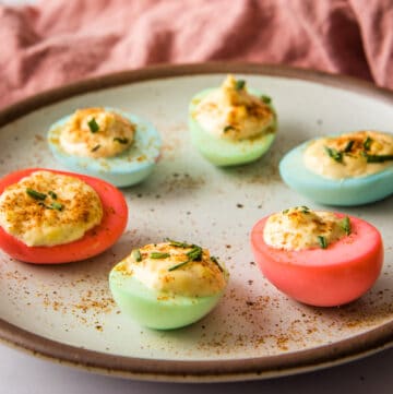 Close up of colored deviled eggs on a plate, with pink napkin in background.