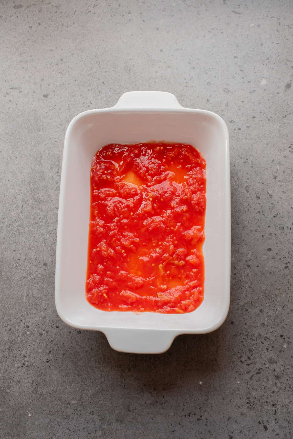 An overhead image of spreading a layer of marinara sauce on a baking sheet.
