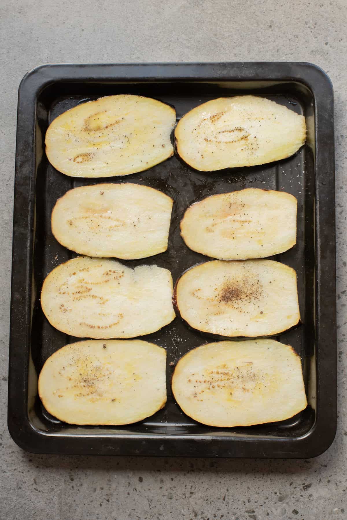 An overhead image of layering eggplant slices on a baking sheet.