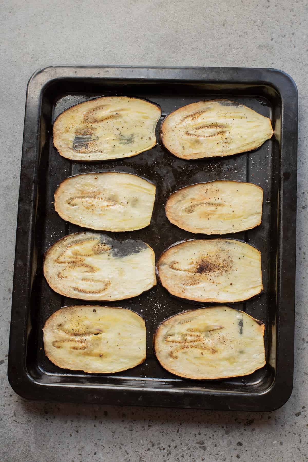 An overhead image of of eggplant slices roasted on a baking sheet.