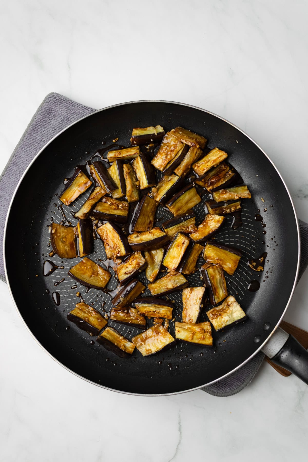 An overhead image of stir frying the eggplants on a skillet.