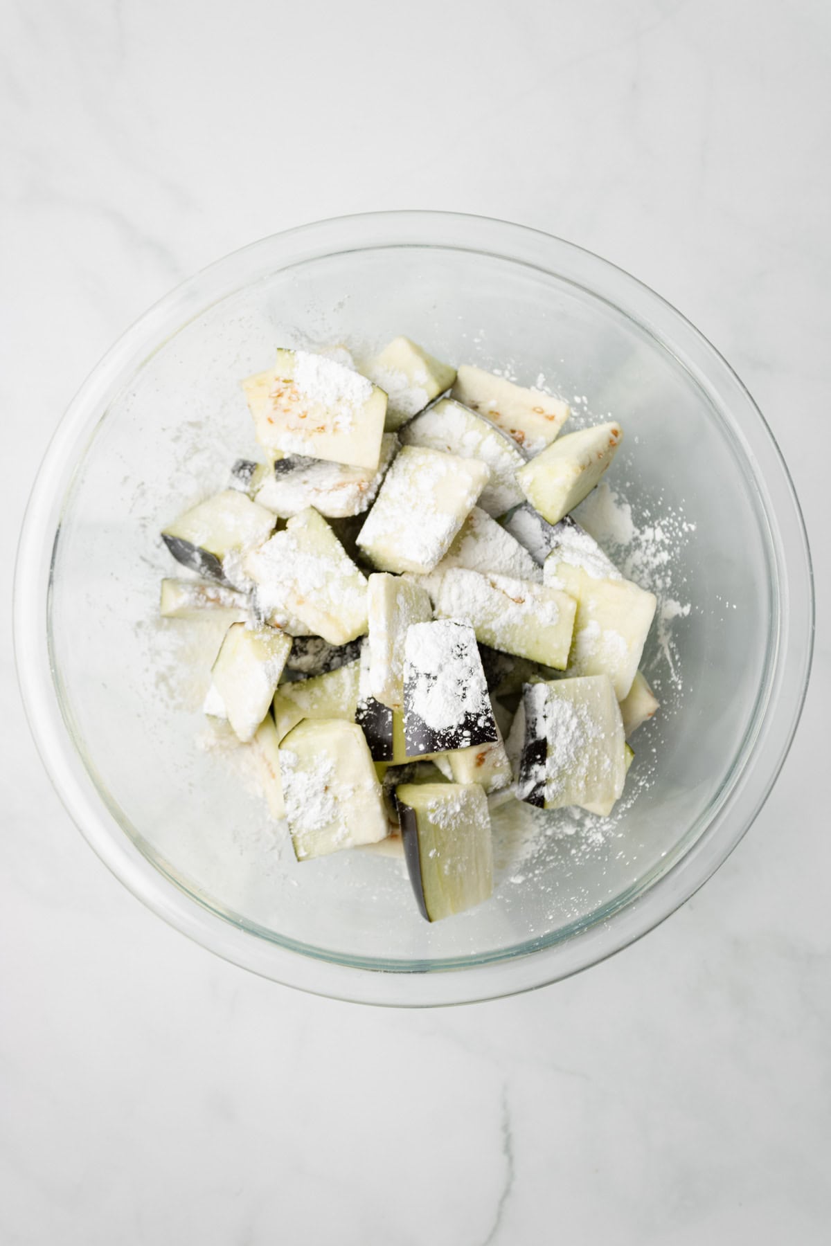 An overhead image of coating the eggplants with cornstarch in a bowl.