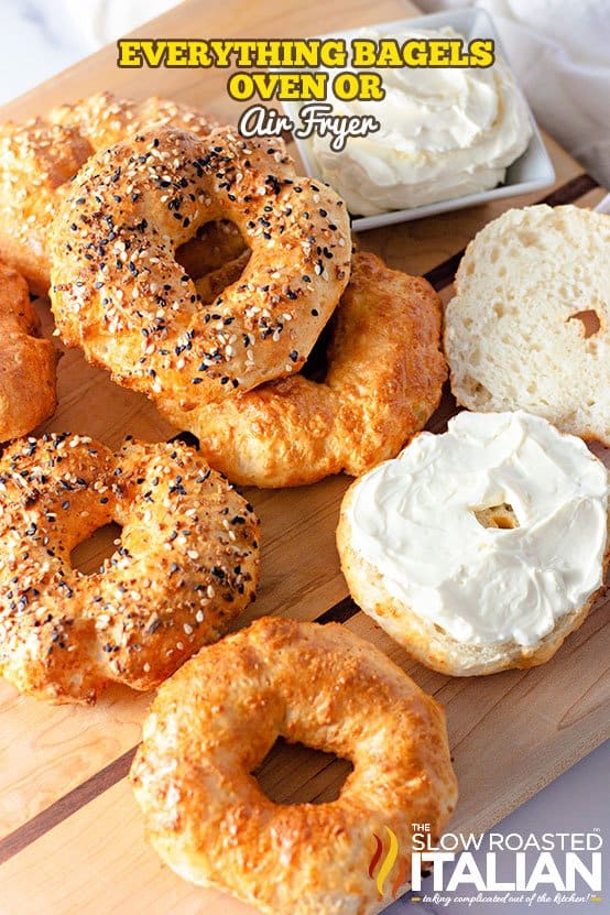 An overhead view of several everything bagels placed on a wooden board.
