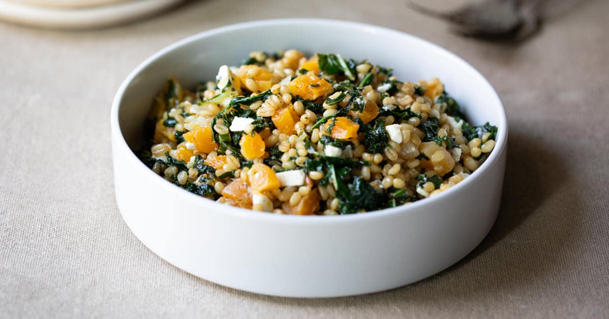 A close-up view of a white serving dish with kale and farro salad.