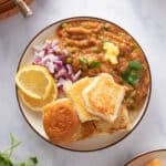 Plate of pav bhaji with rolls, bhaji, red onions, lemon wedges and garnished with cilantro
