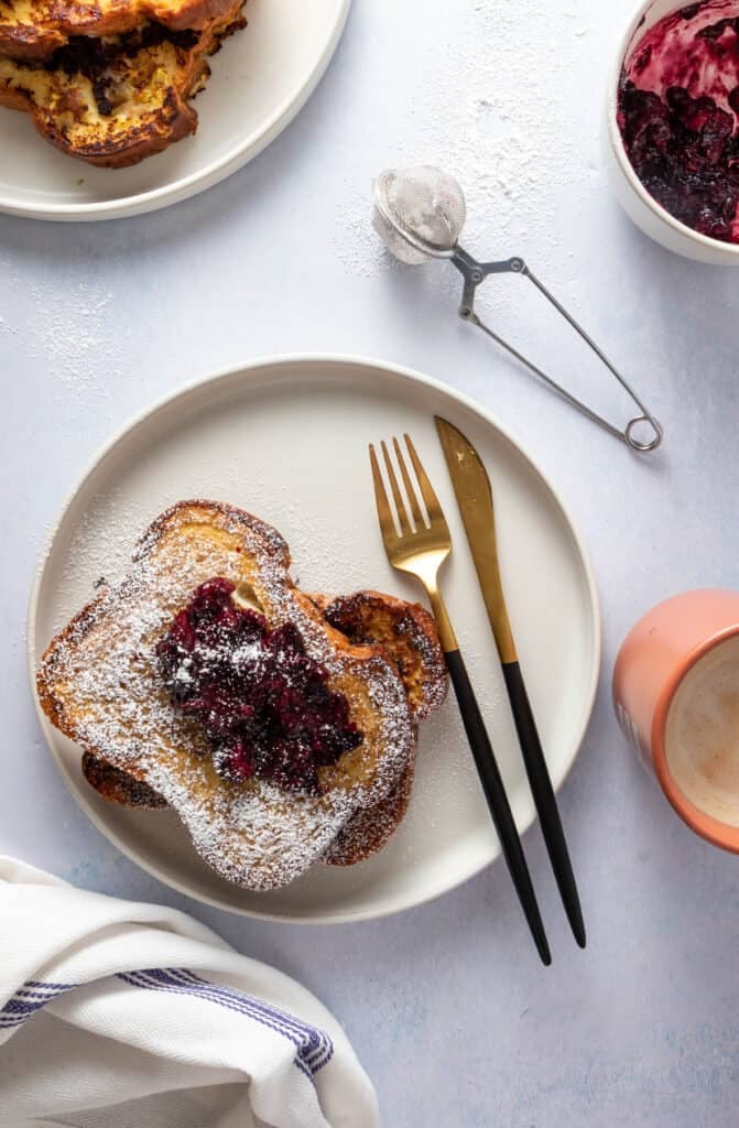 Plate of French toast with berry compote and utensils - coffee, berry compote and other toasts on the side