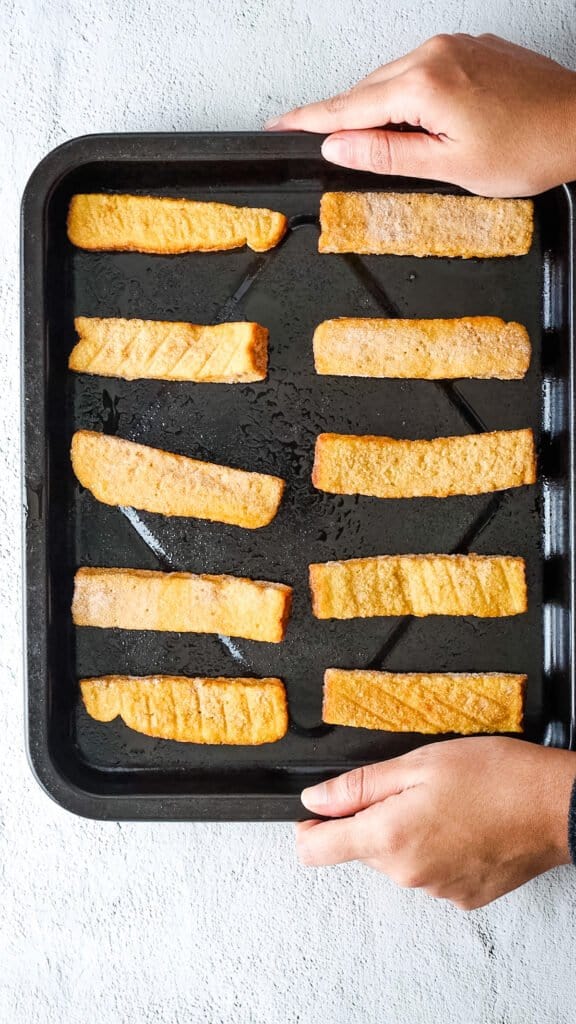 Frozen French toast sticks arranged on air fryer tray before air frying 