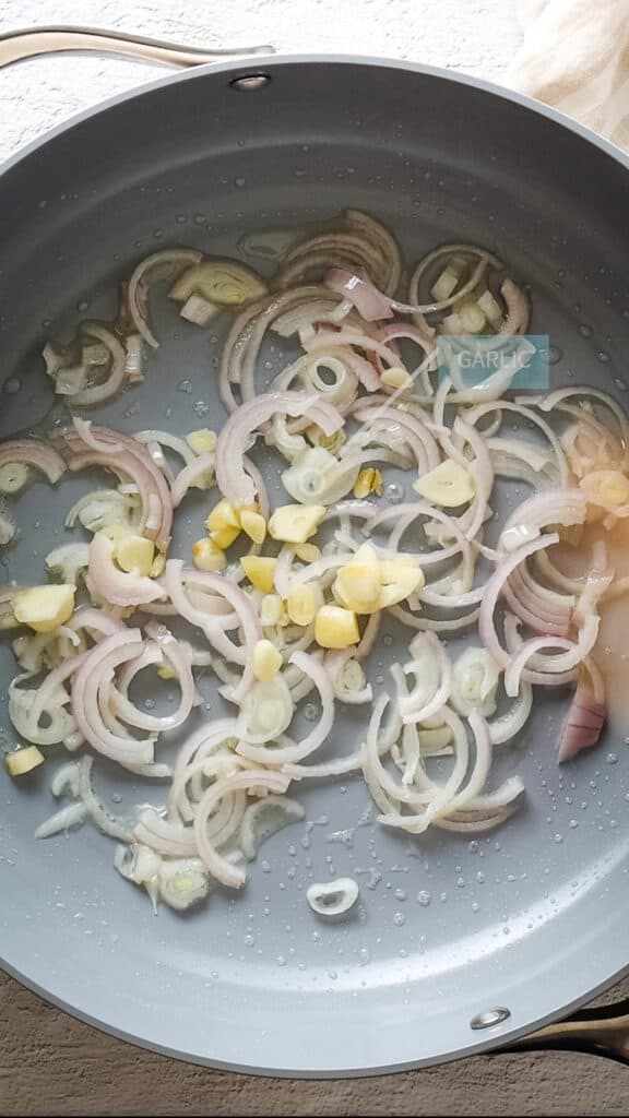 Close up of garlic being added to saucepan with fried shallots.