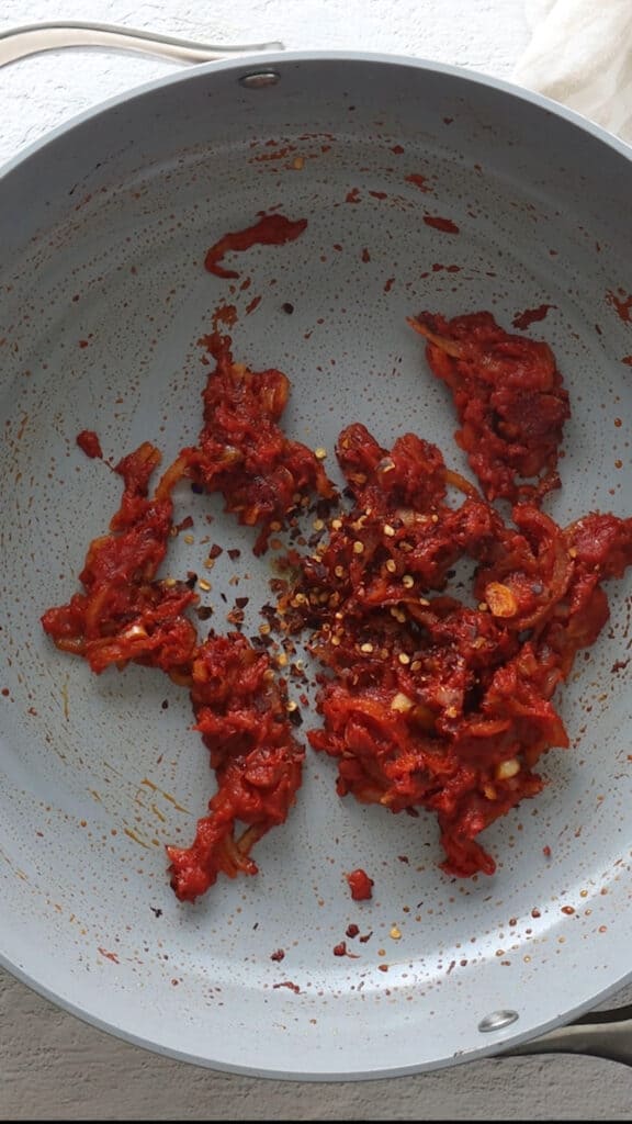 Close up of red pepper flakes added to saucepan.