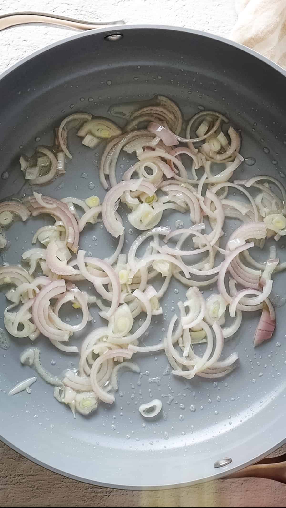 Close up of saucepan with shallots being fried in oil.