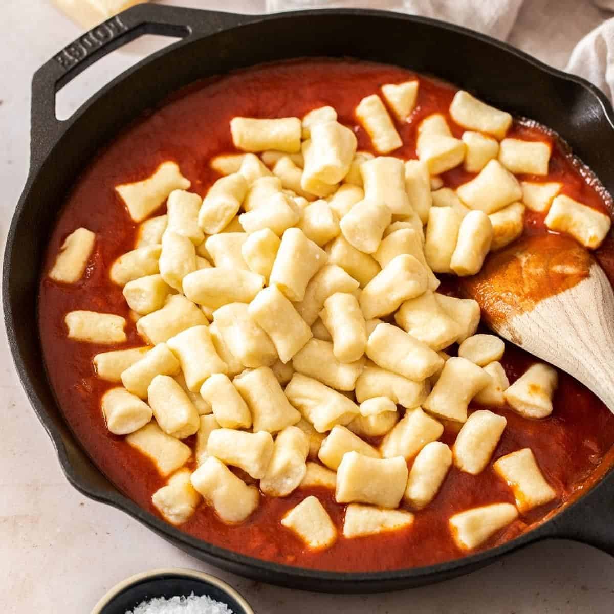 Overhead view of Gnocchi di Ricotta on top of the tomato sauce with wooden spoon.