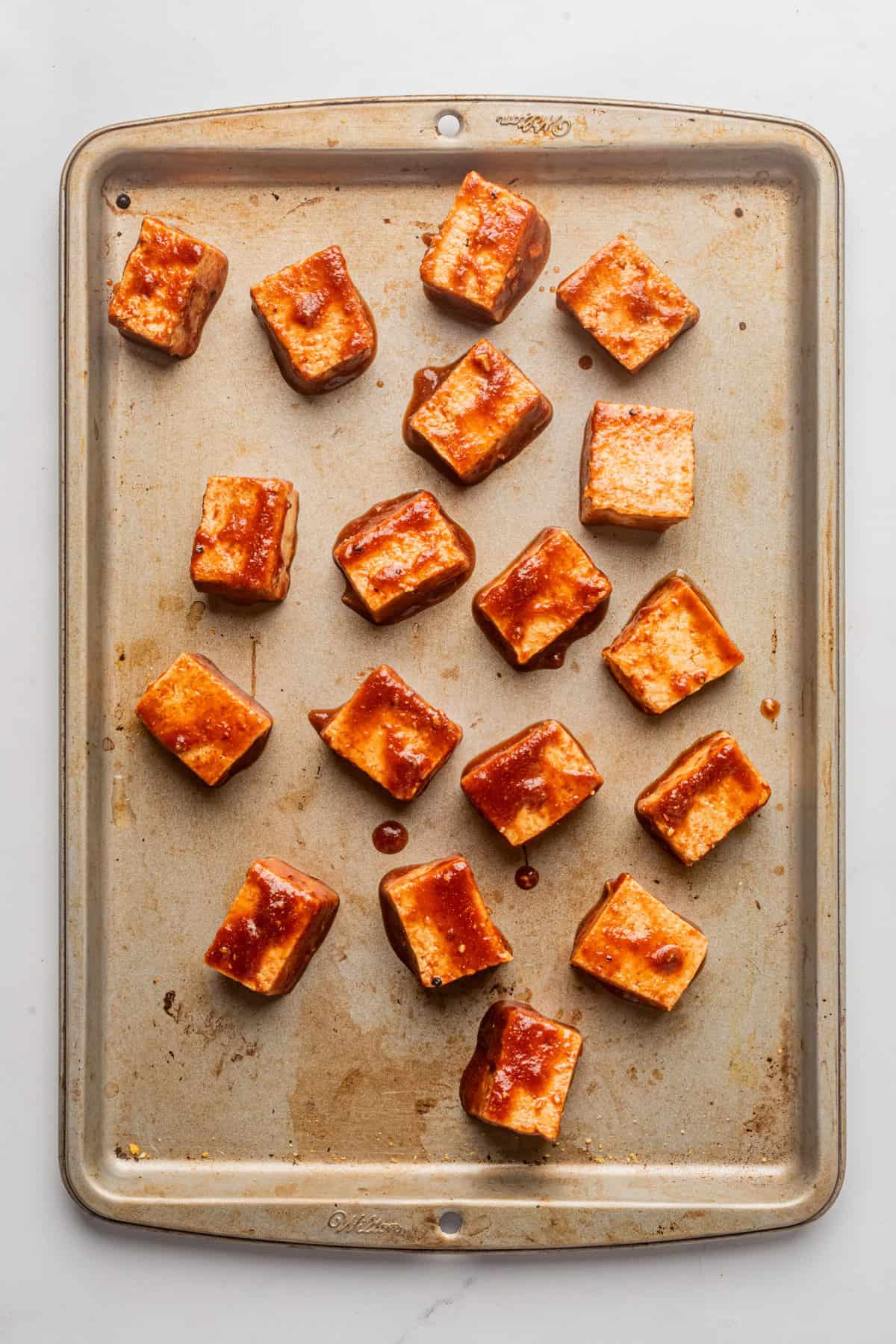 An image of gochujang sauce-coated tofu evenly spread out in a baking pan.