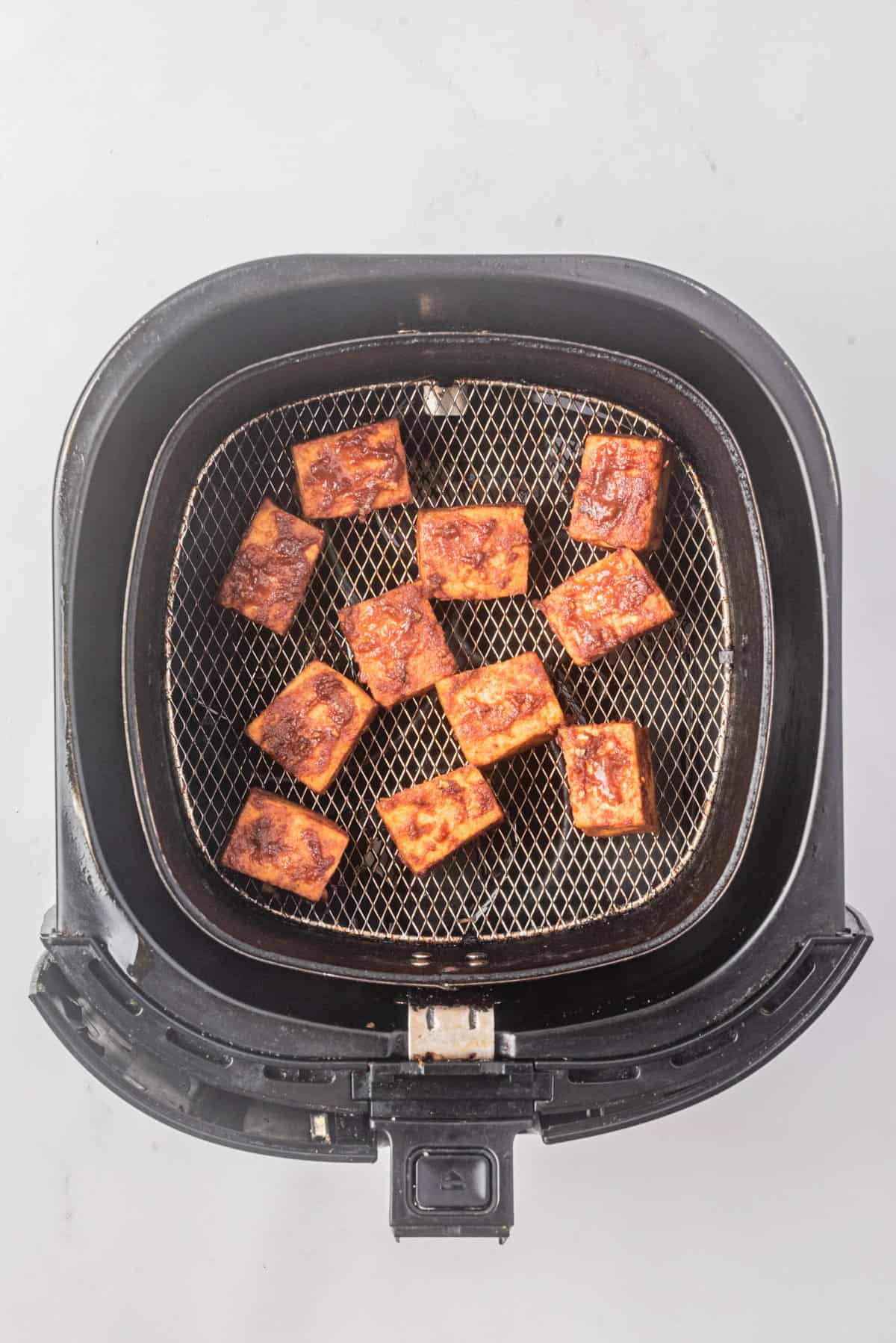 An overhead image of gochujang sauce-coated tofu in an air fryer.