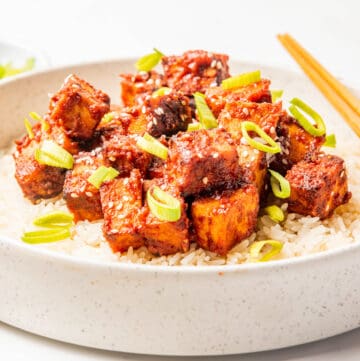 A close up image of a gochujang tofu rice bowl with chopsticks on the side.
