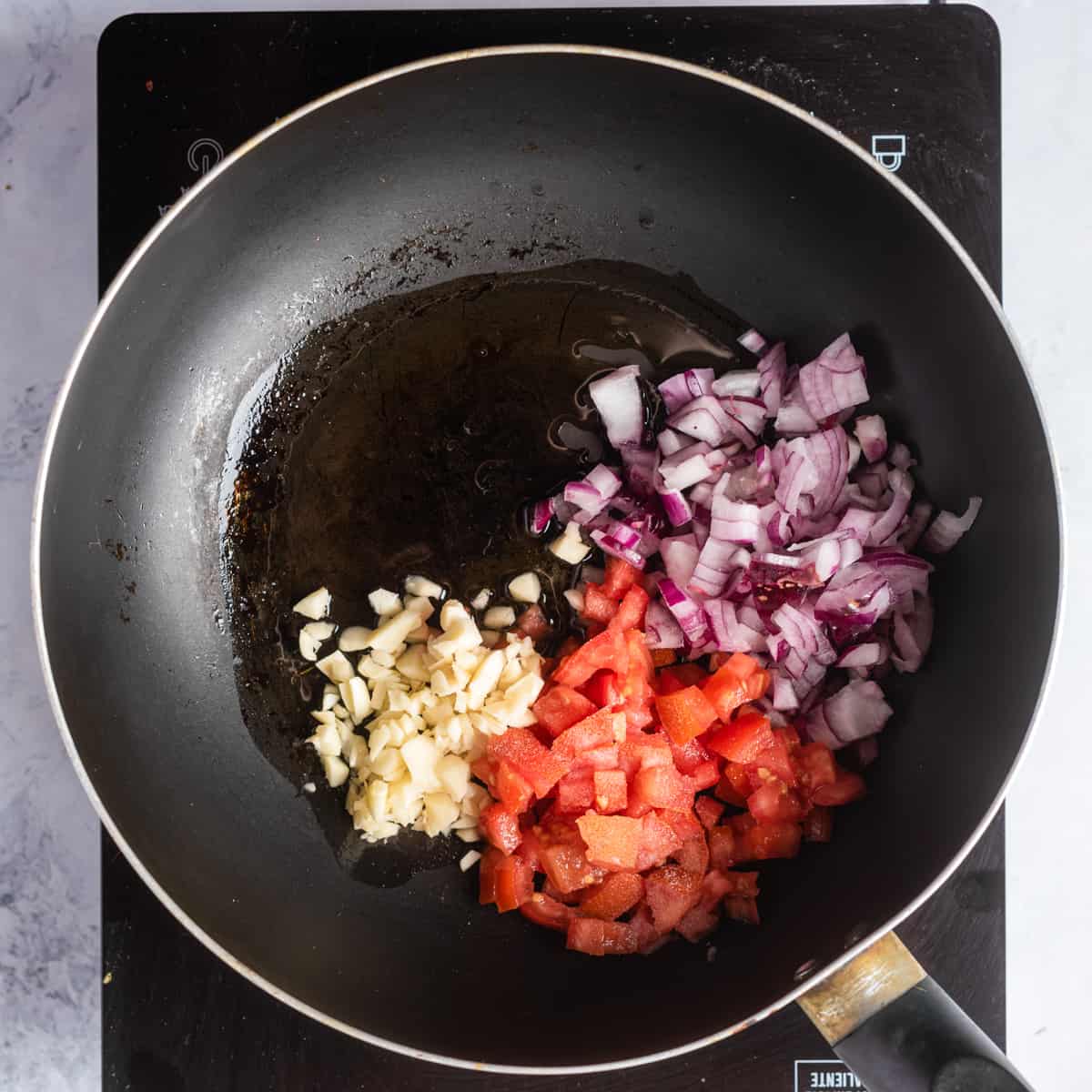 Overhead view of a skillet pan with chopped onions, oil, garlic, and salt.