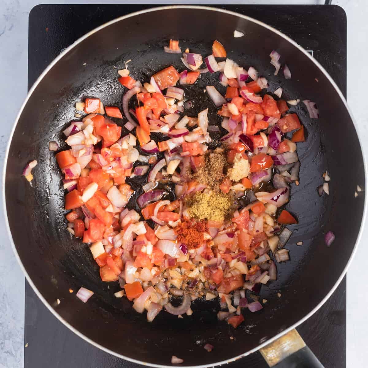 Overhead view of a skillet pan with sauteed onions, oil, and garlic added with cumin powder and paprika.