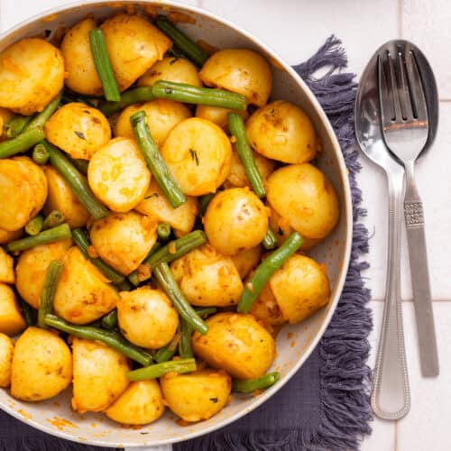 An overhead image of green beans and potatoes in a pan with a fork and spoon on the side.