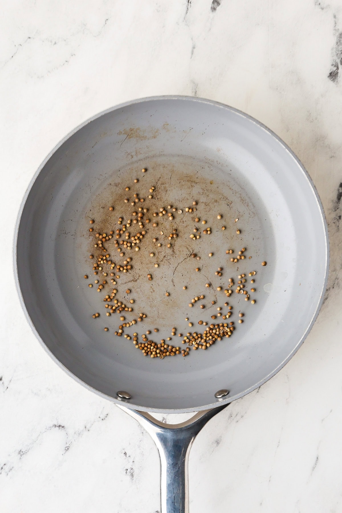 Coriander seeds being toasted in a pan.