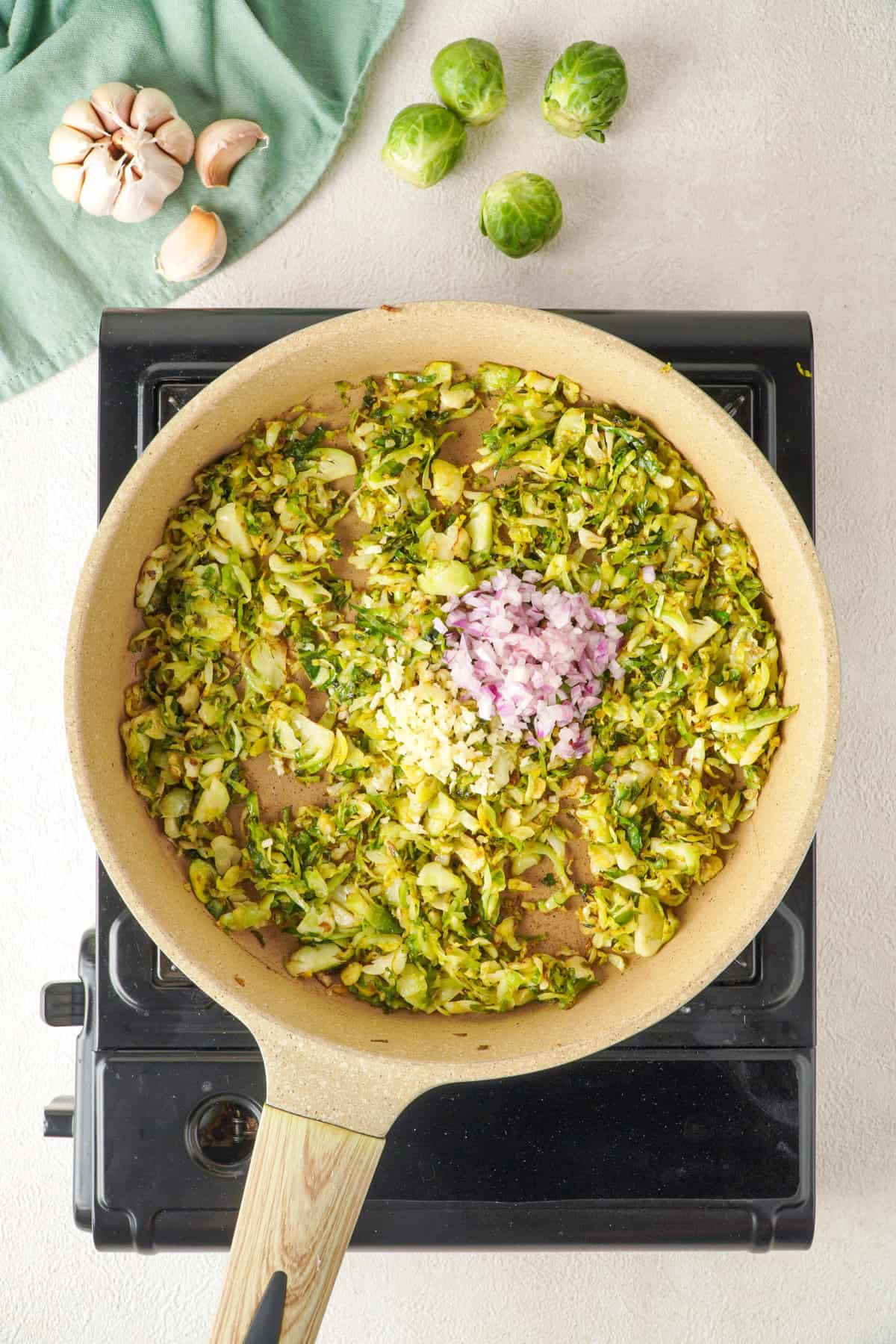 Overhead view of shallots added to skillet with shaved Brussels sprouts.