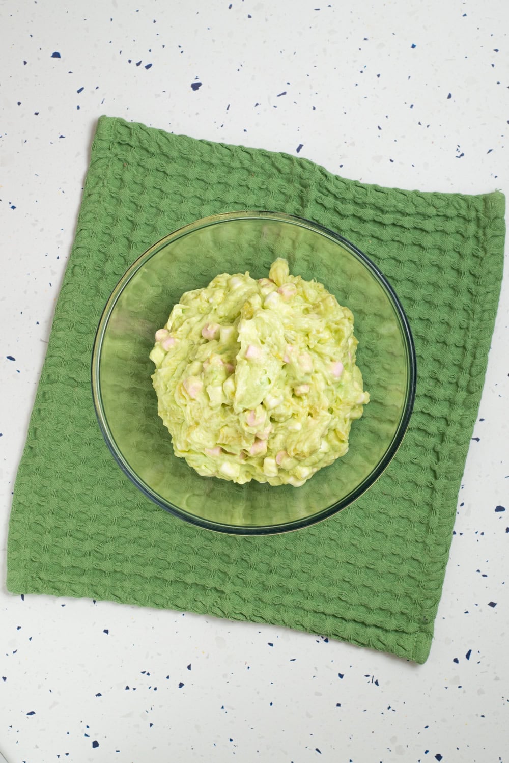 Bright green Grinch fluff mixed with mini marshmallows in a glass bowl.