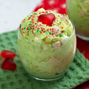 Green Grinch fluff topped with red candy heart and red and green sprinkles in a clear glass.