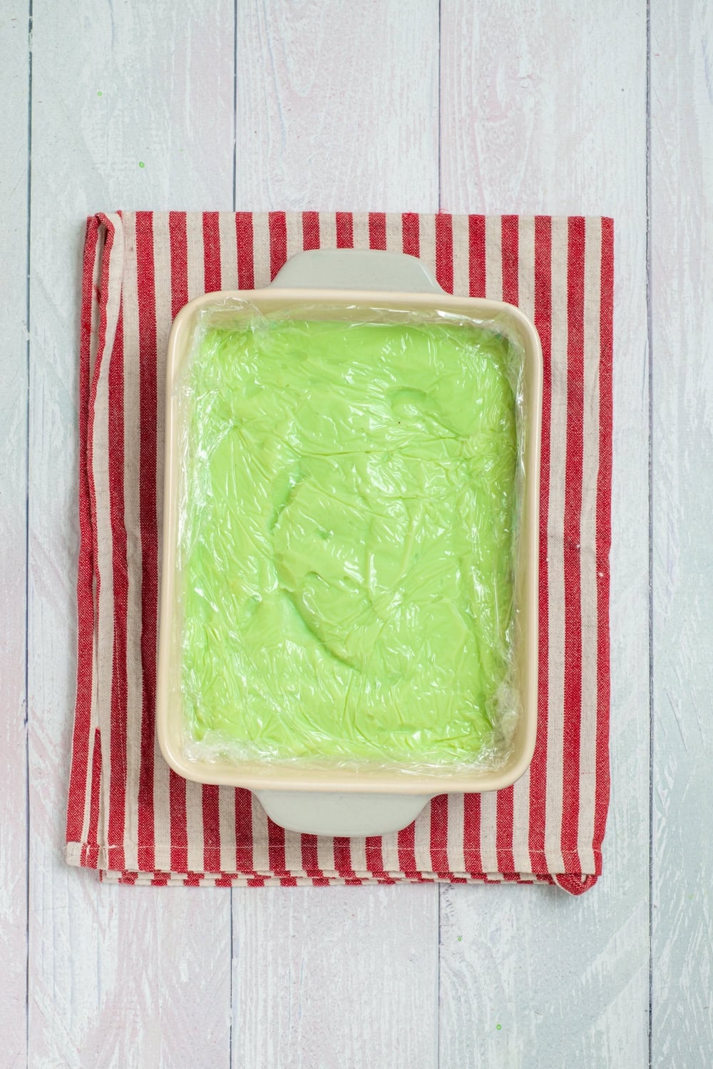 Green pudding covered with plastic wrap before chilling.