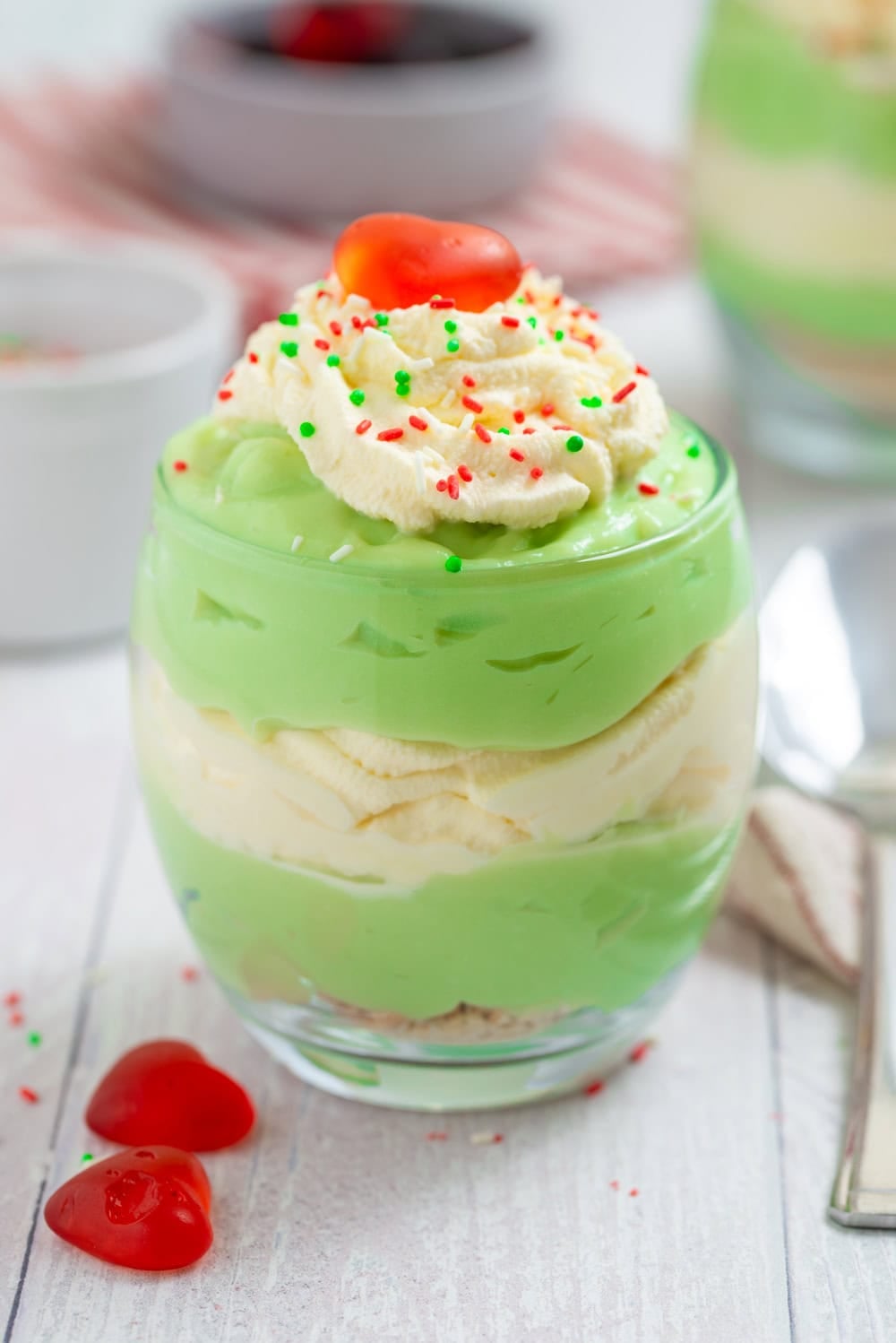 Layered Grinch Who Pudding topped with whipped cream, Christmas sprinkles, and a red candy heart.