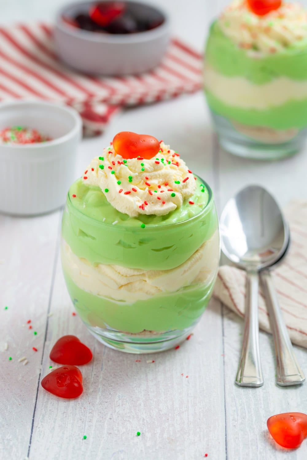 Grinch Who Pudding in a glass with layers of green pudding and whipped cream, Christmas sprinkles, and a red candy heart.