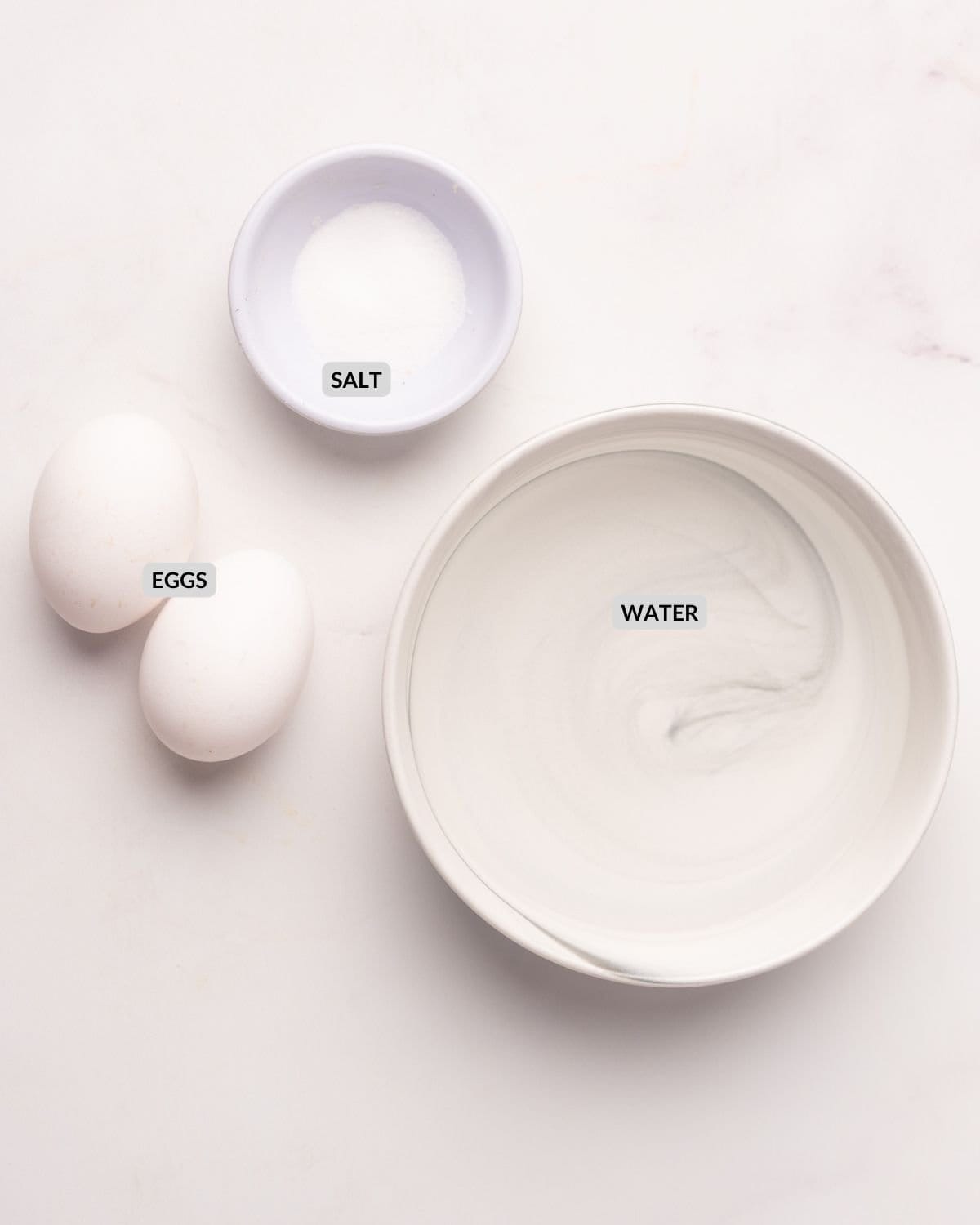 An overhead image of two eggs, salt in a small bowl, and water in another bowl.