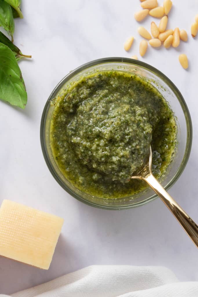 close up of basil pesto with a spoon in the bowl, parmesan for garnish on the side