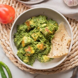 An overhead image of high protein palak paneer in a bowl with naan on the side.