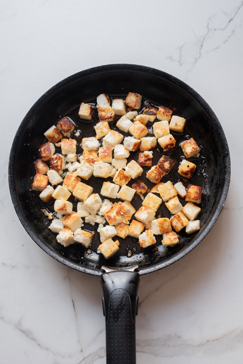 An overhead image of cooking the paneer on a cast iron skillet.
