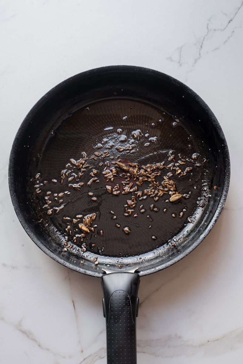 An overhead image of sizzling cardamom pods and cumin seeds.
