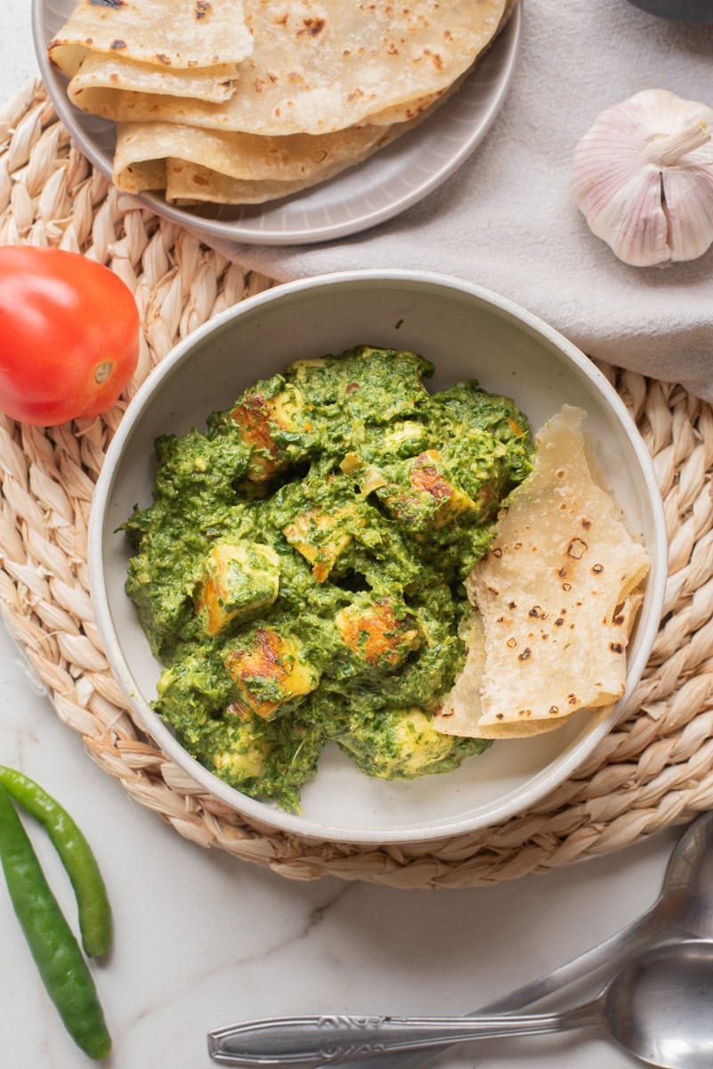 An overhead image of high protein palak paneer in a bowl with naan on the side.