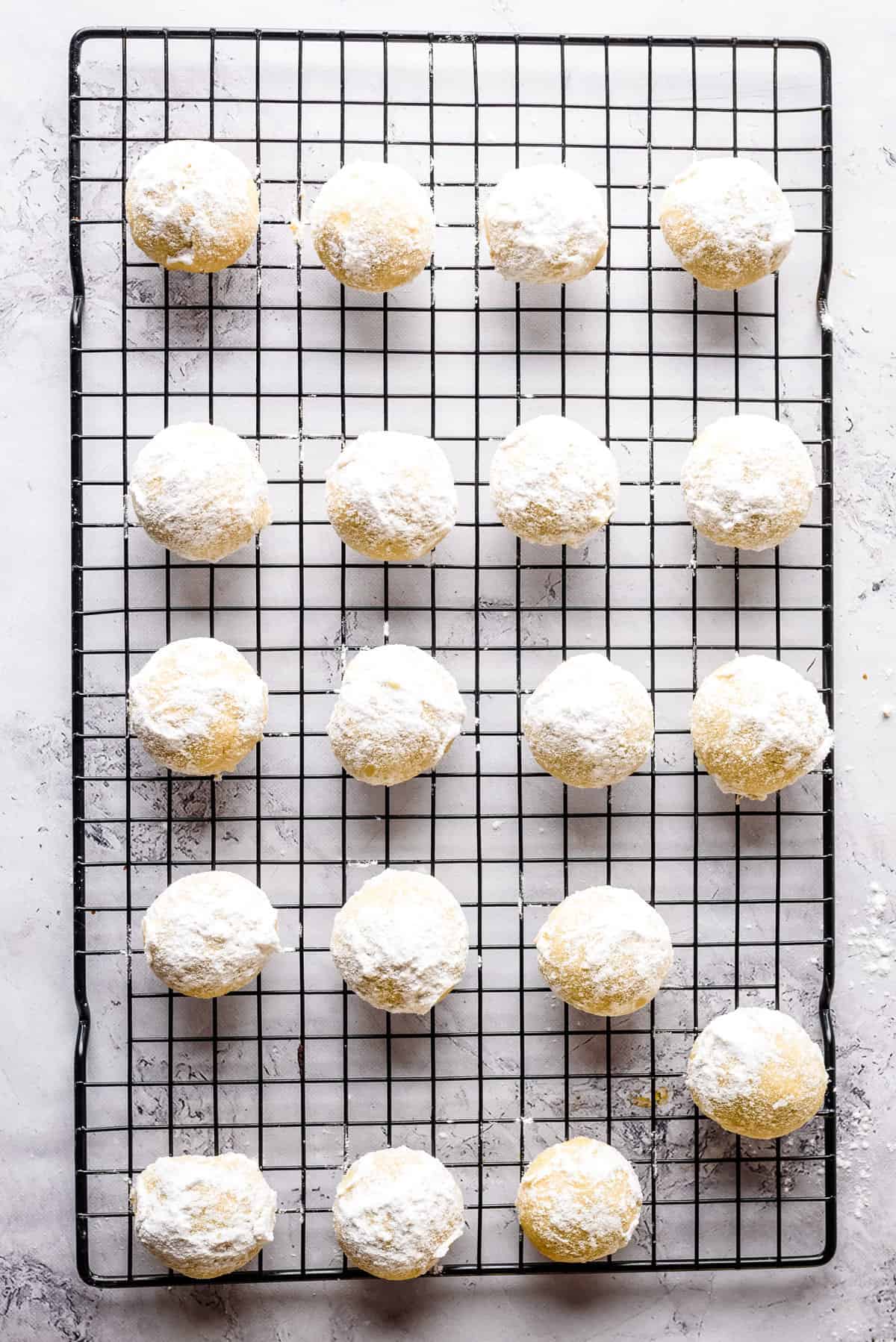 Overhead view of holiday butter cookies after being dipped in powdered sugar, on black wire rack.