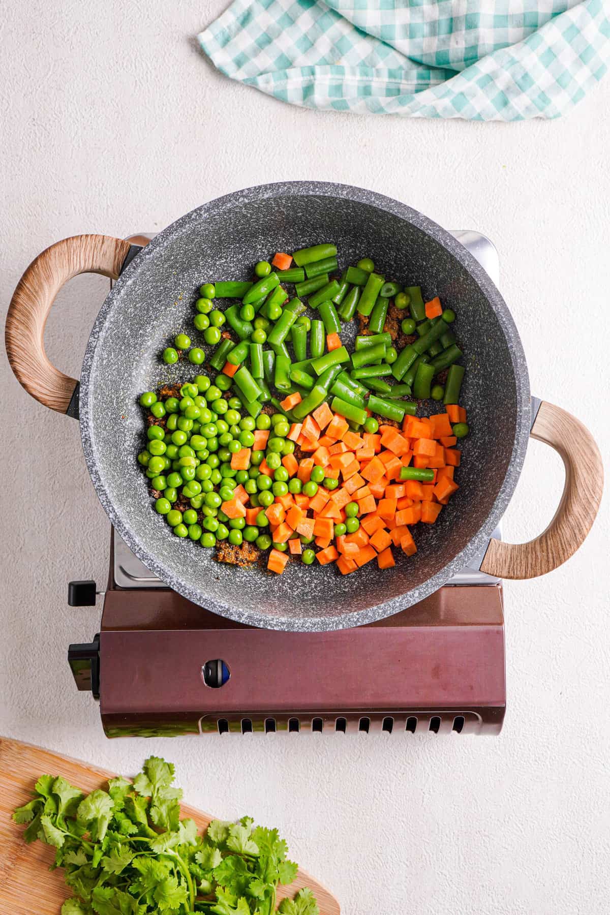 Overhead view of vegetables added to the skillet with spices.