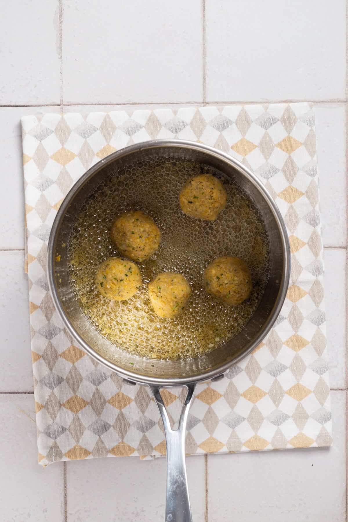 An overhead image of falafel balls being fried in a deep frying pan filled with oil.
