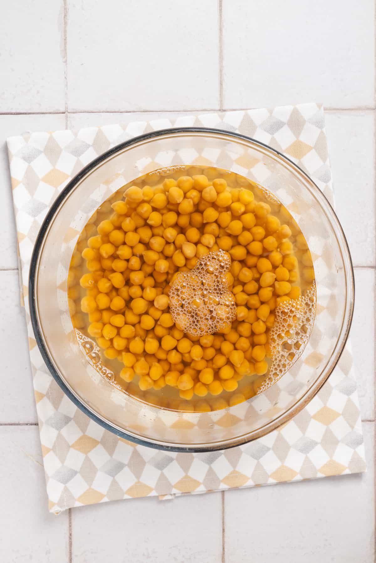 An image of chickpeas soaked in water in a clear bowl .