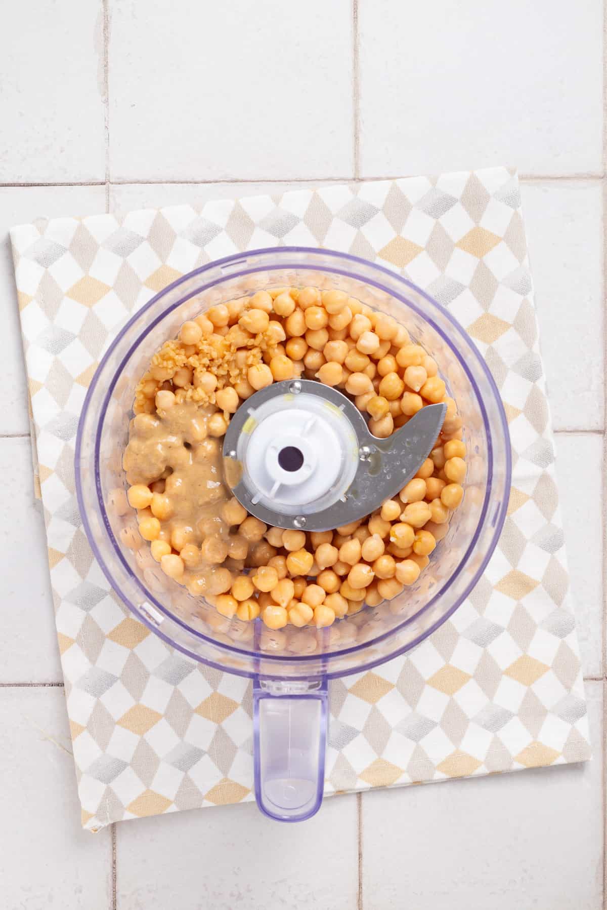 An overhead image of chickpeas, lemon, tahini, garlic, and olive oil in a food processor, before being processed.