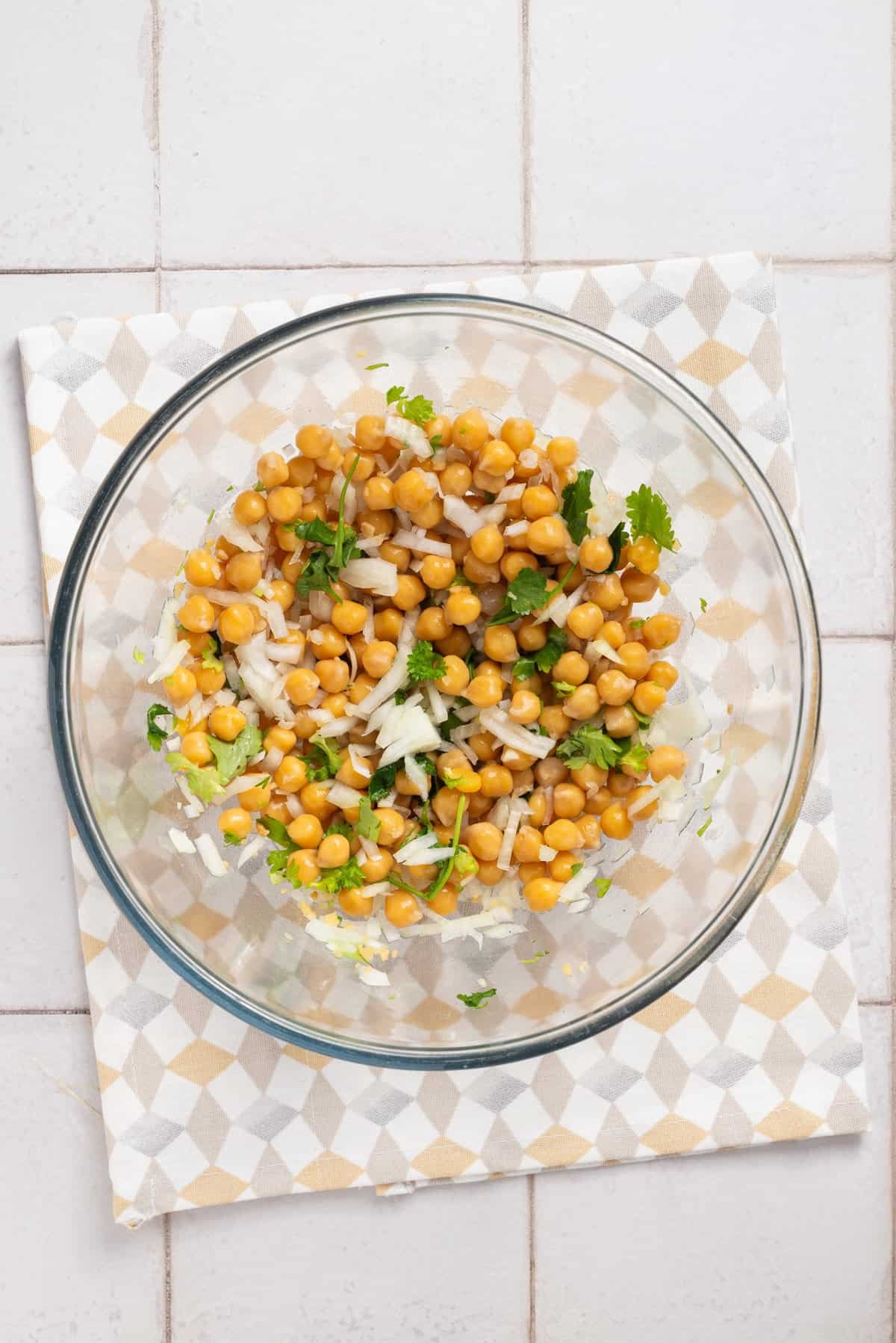 An overhead image of chickpeas and herbs in a large clear bowl.