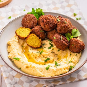 A close up image of falafels arranged on top of a bowl filled with hummus.