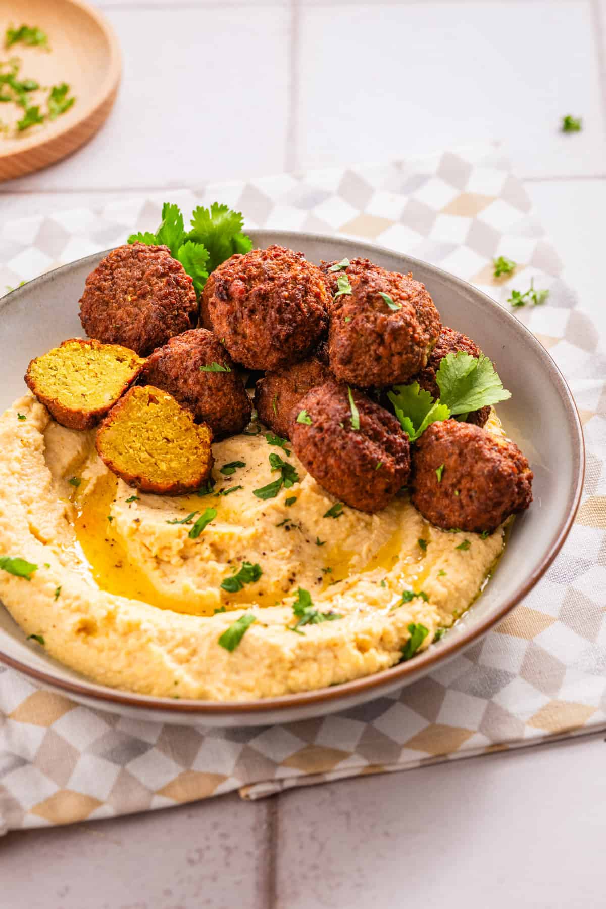 An image of falafels arranged on top of a white bowl filled with creamy hummus.