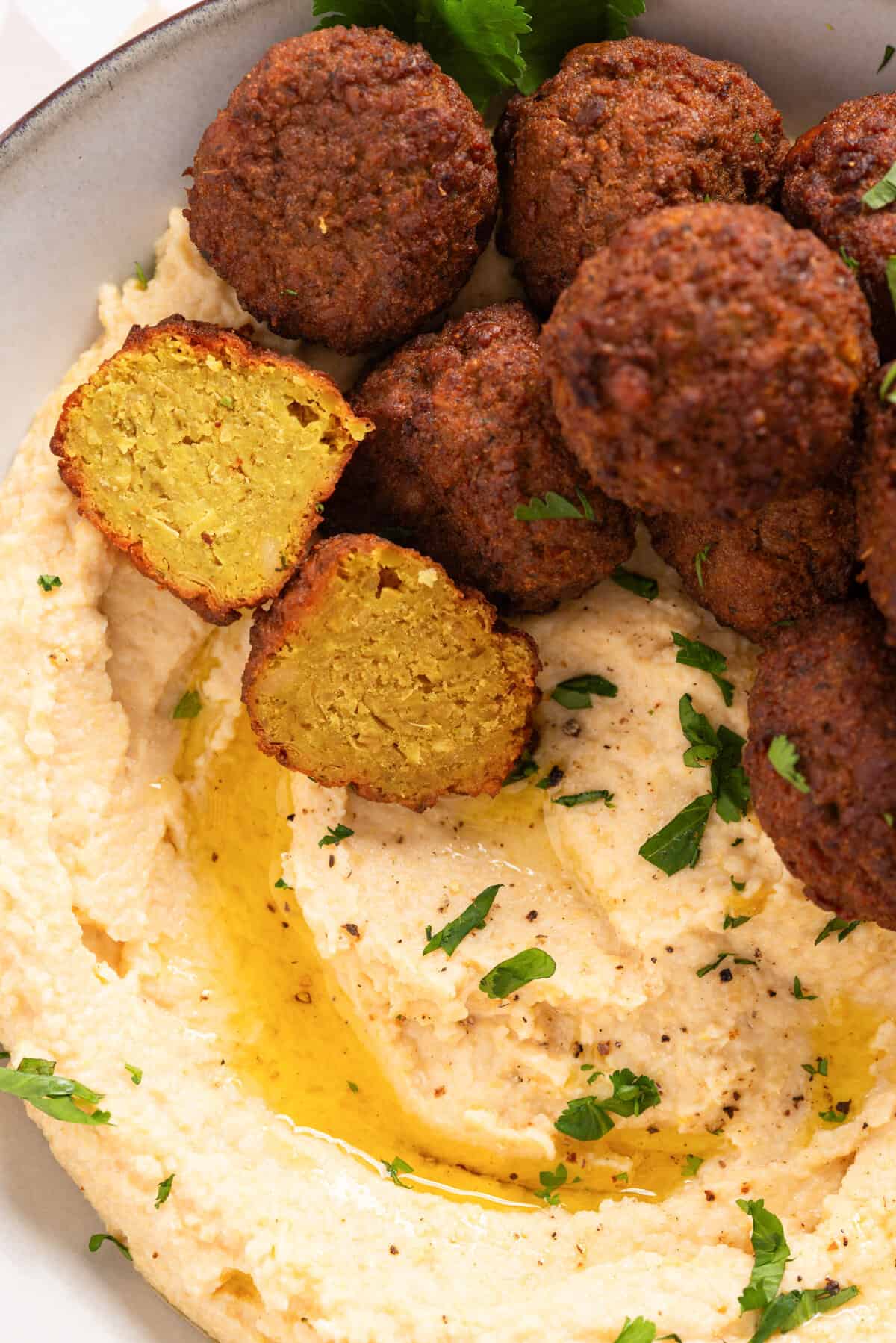 A close up image of falafels on top of a bowl filled with hummus.